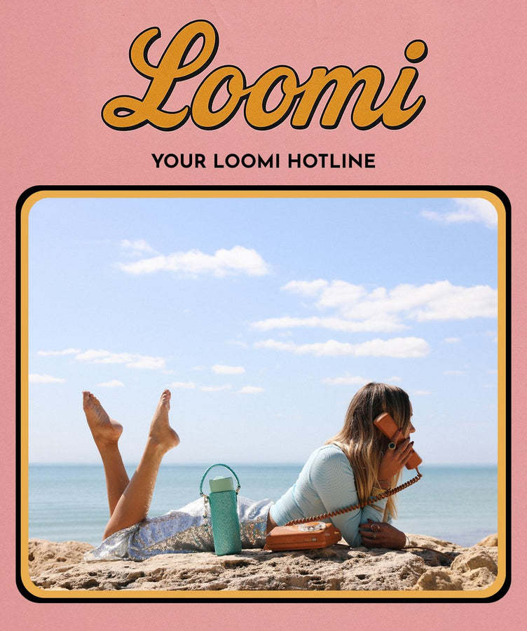 Person lying on a rock by the ocean with a Loomi water bottle, promotional text for Loomi hotline.