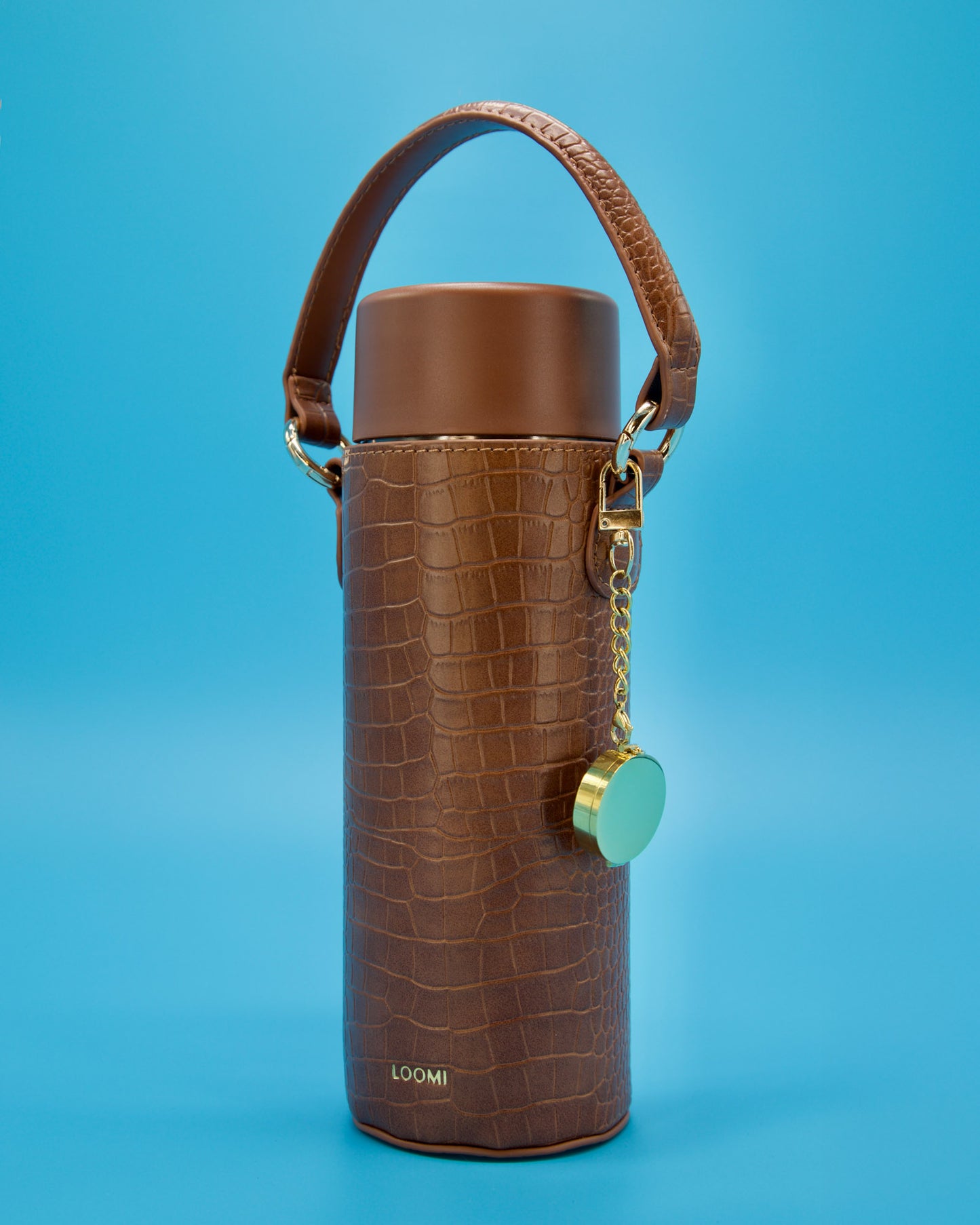 a gold circle locket on a 3 cm gold chain with a hot ink lip balm inside Featured on a blue background clasped on the side of a brown faux croc cover water bottle