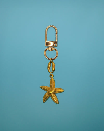 Gold starfish charm with cowrie link on a gold clip, photographed on a blue background — Loomi water bottle charm.