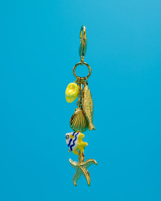 Gold charm with gold fish, gold clamshell yellow blue and white ceramic fish and gold starfish hanging down and blue background