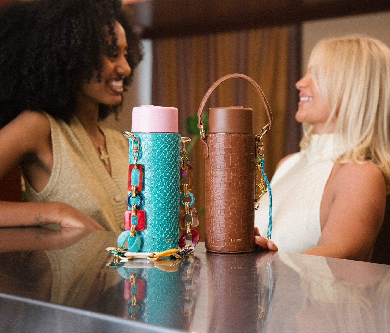 Two women sitting at a table with colorful water bottles in front of them.