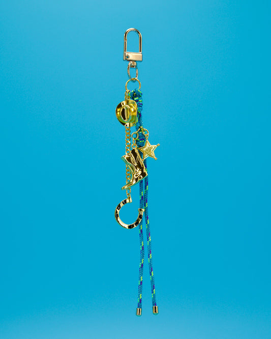 gold key charm with thin blue and green rope hanging down with gold boot a gold cowboy hat and a gold horseshoe hanging at different intervals on blue background 